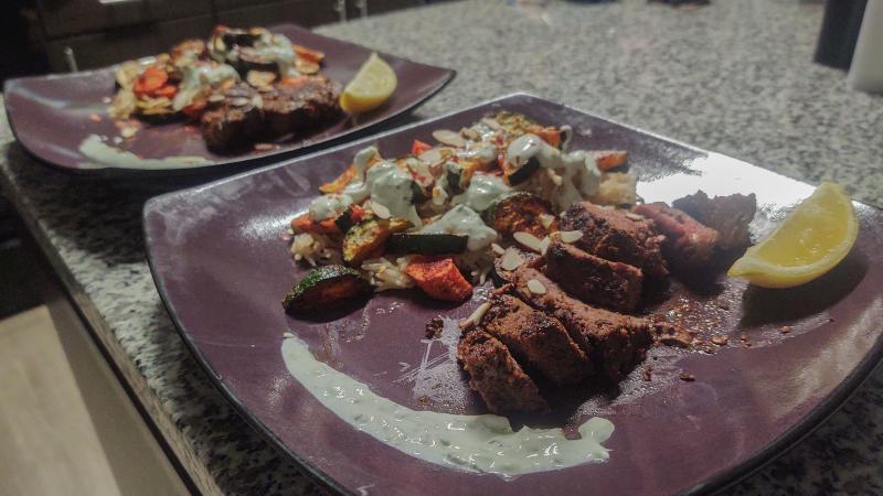 Two purple plates with cut steak, rice and roasted vegetables on a kitchen counter.