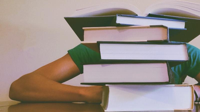 Stressed student buried behind textbooks.