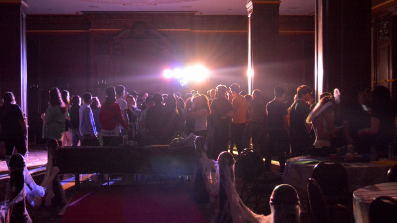 Students dance near a DJ, with strobe lights shining at the camera