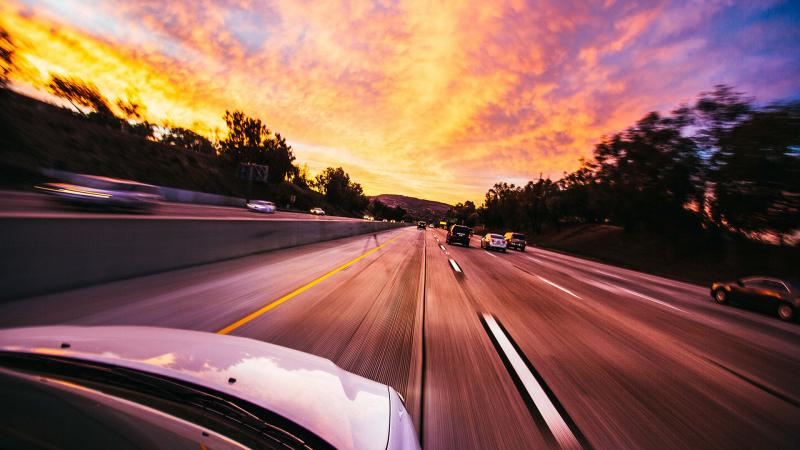 Car speeding down a highway into the sunset