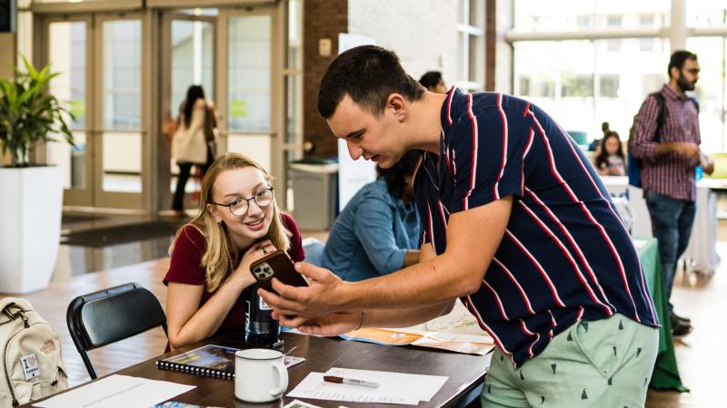 Two students look at a phone at the Student Organization Fair.