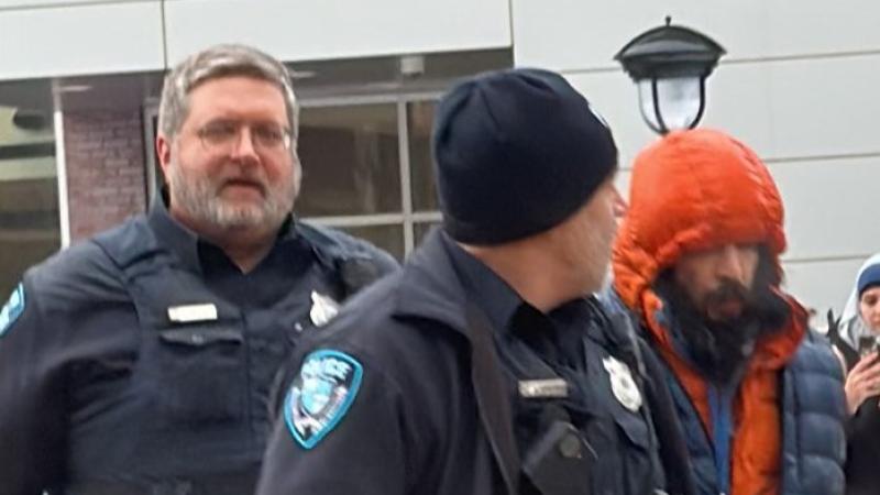Two officers arrest a man in an orange puffer jacket.