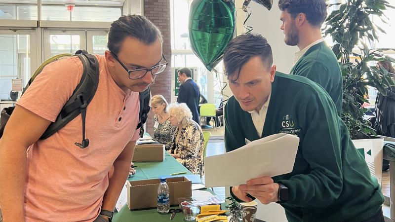 Both a student in an orange shirt, left, and a career development coach in a green cardigan, right, lean over a table sharing a white paper.