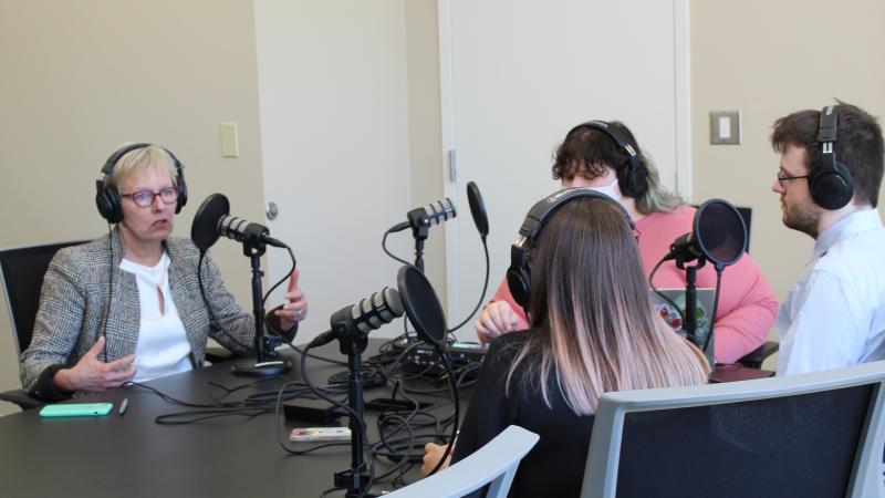 CSU Presudent, Laura Bloomberg Ph.D., left, sits in front of a microphone at a black table across from students from the student newspaper for an interview.