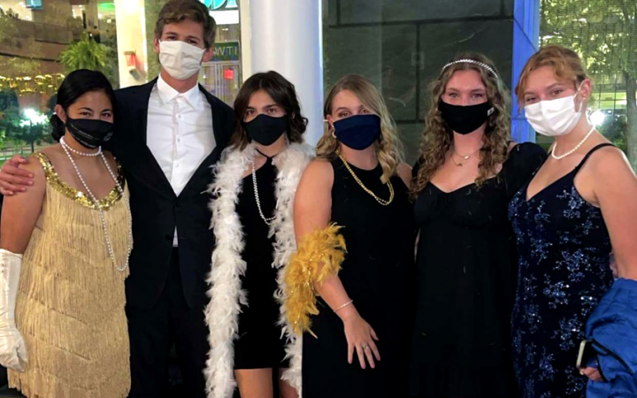 six people dressed in 1920s outfits, wearing masks