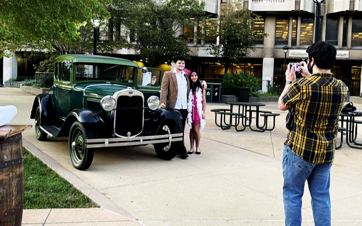 one student takes a photo of two other students next to Model A Ford