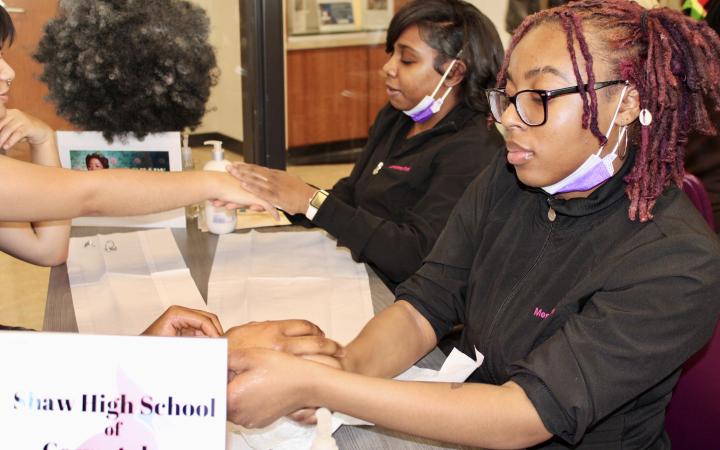 Two students from Shaw High School’s Cosmetology Department give hand and arm massages  at the Let Freedom Ring Solidarity day exhibit in Berkman Hall on Thursday, Feb. 1.