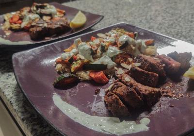 Two purple plates with cut steak, rice and roasted vegetables on a kitchen counter.