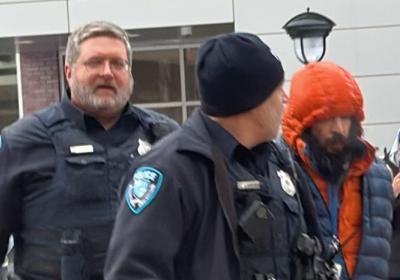 Two officers arrest a man in a puffer jacket. 