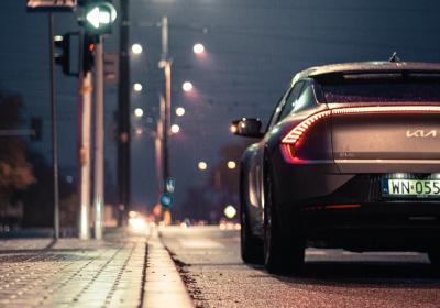 A Kia vehicle waits at a traffic light on a dark road.