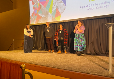 A member of the Cleveland International Film Festival stands on stage with three filmmakers.