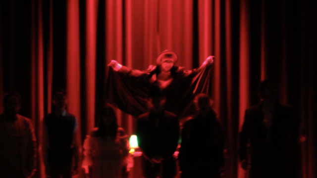 The Phantom stands over the cast, bathed in red light.